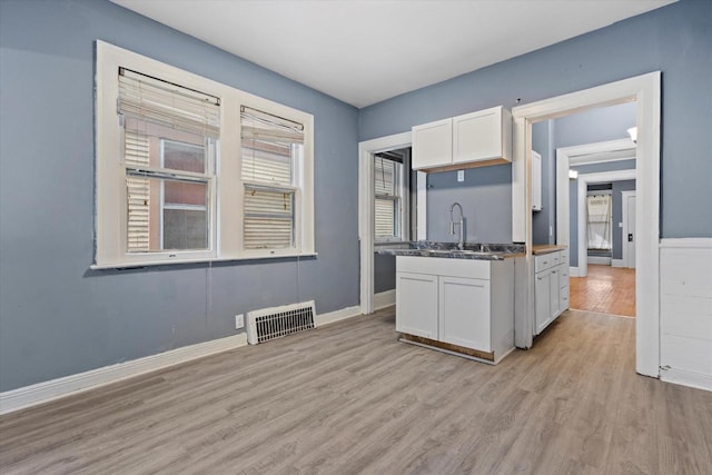 kitchen featuring baseboards, visible vents, a sink, white cabinetry, and light wood-type flooring