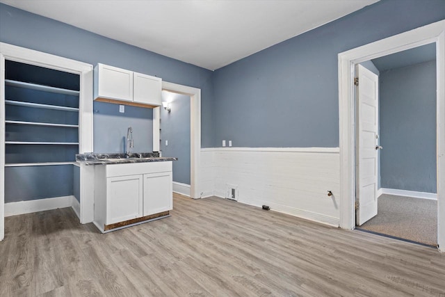 kitchen with a sink, light wood-style flooring, wainscoting, and white cabinetry