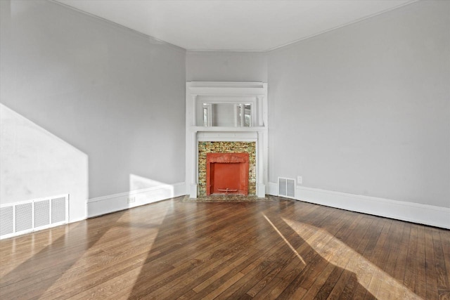 unfurnished living room with a tiled fireplace, visible vents, baseboards, and wood-type flooring