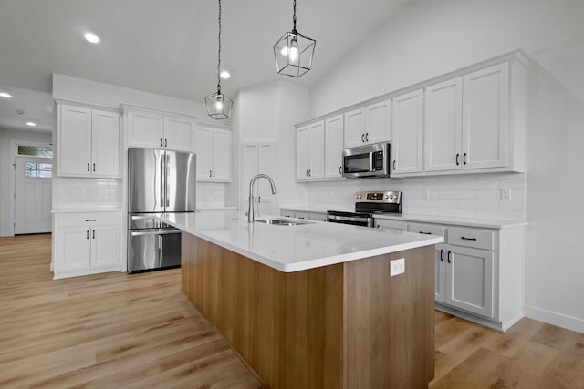 kitchen featuring light wood finished floors, a sink, decorative light fixtures, appliances with stainless steel finishes, and a kitchen island with sink