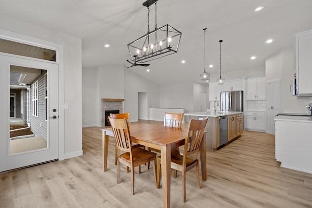 dining area with recessed lighting, lofted ceiling, a stone fireplace, and light wood finished floors