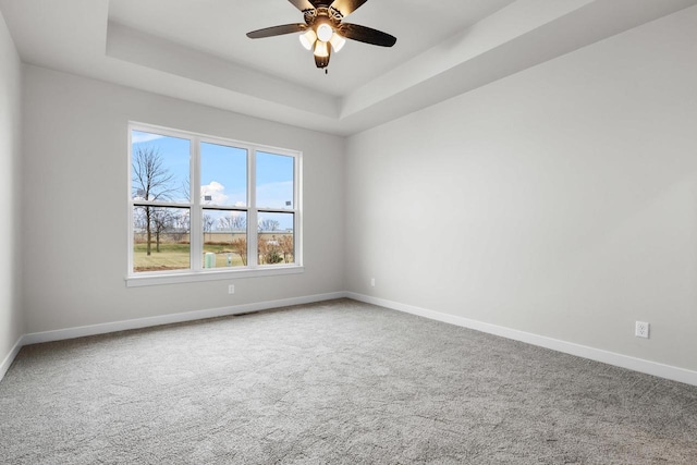 carpeted spare room featuring a tray ceiling, a ceiling fan, baseboards, and visible vents