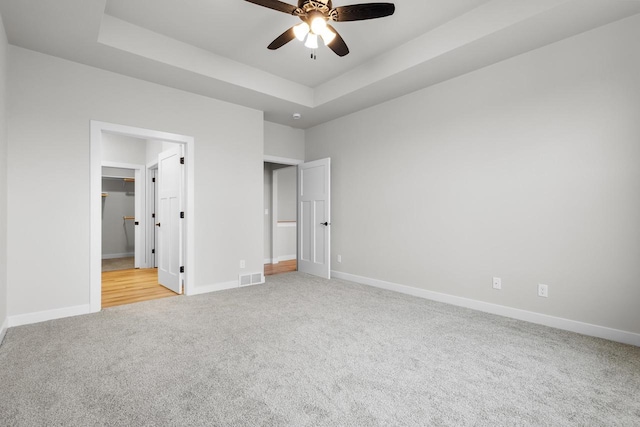 unfurnished bedroom featuring light carpet, visible vents, baseboards, and a tray ceiling