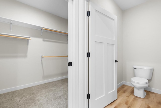 bathroom with a walk in closet, toilet, and baseboards