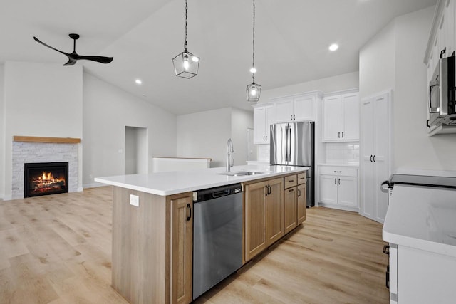 kitchen with light wood finished floors, a sink, lofted ceiling, stainless steel appliances, and a kitchen island with sink