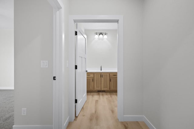 corridor featuring light wood-style flooring, baseboards, and a sink