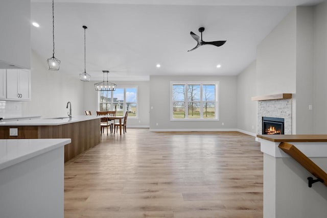 unfurnished living room featuring recessed lighting, a sink, a stone fireplace, ceiling fan, and light wood-type flooring