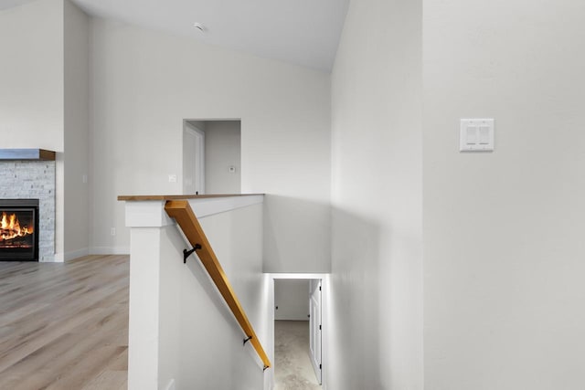 staircase featuring a stone fireplace, wood finished floors, baseboards, and high vaulted ceiling