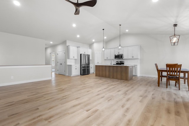 kitchen featuring open floor plan, light countertops, light wood-type flooring, appliances with stainless steel finishes, and a kitchen island with sink