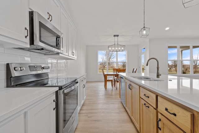 kitchen with a sink, tasteful backsplash, light wood-style floors, appliances with stainless steel finishes, and light countertops