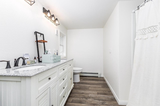 bathroom with toilet, double vanity, baseboard heating, wood finished floors, and a sink