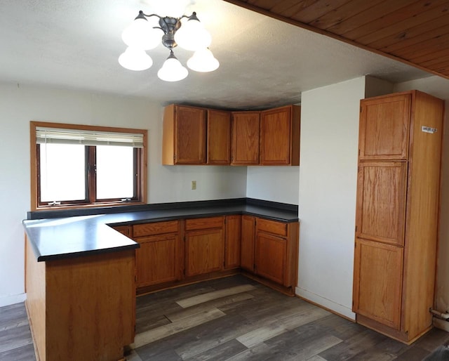 kitchen with dark countertops, brown cabinets, a peninsula, an inviting chandelier, and wood finished floors