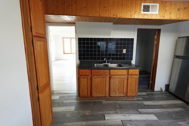 kitchen featuring visible vents, a sink, tasteful backsplash, dark countertops, and freestanding refrigerator