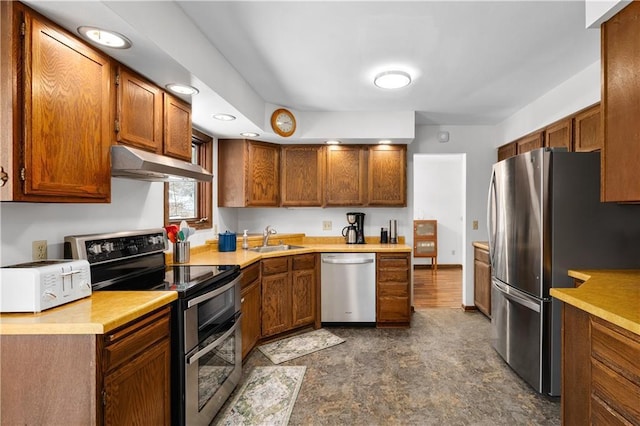 kitchen with a sink, light countertops, under cabinet range hood, appliances with stainless steel finishes, and brown cabinets