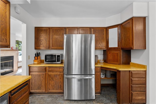 kitchen with brown cabinetry, a glass covered fireplace, stainless steel appliances, and light countertops