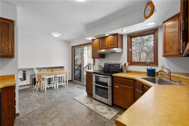 kitchen with brown cabinets, a sink, double oven range, under cabinet range hood, and light countertops