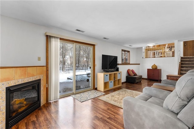 living room with a tiled fireplace, stairs, wood finished floors, and visible vents