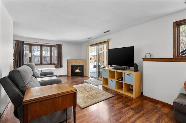 living room featuring a tiled fireplace, visible vents, dark wood-type flooring, and baseboards