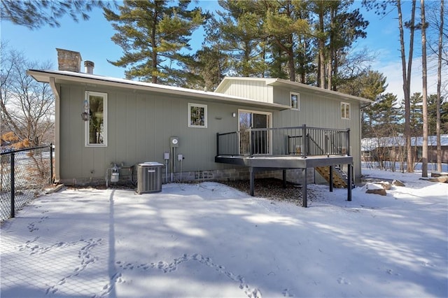 snow covered rear of property with a deck, fence, cooling unit, stairway, and a chimney