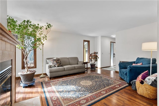 living area with a tiled fireplace, baseboards, and wood finished floors