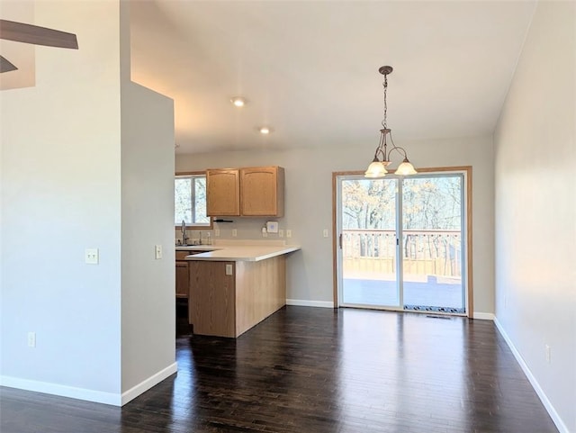 kitchen with baseboards, dark wood finished floors, light countertops, a peninsula, and a sink