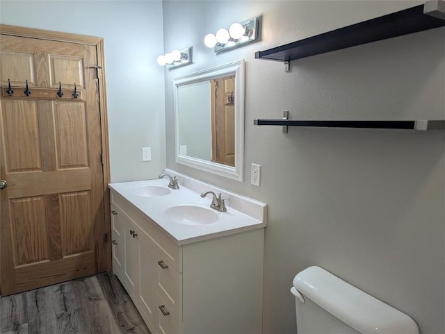 bathroom with double vanity, wood finished floors, toilet, and a sink