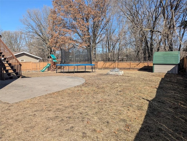 view of yard featuring an outdoor structure, a trampoline, a fenced backyard, and a playground