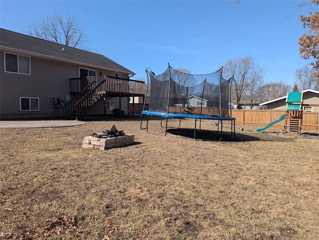 view of play area featuring a trampoline, an outdoor fire pit, fence, a wooden deck, and stairs