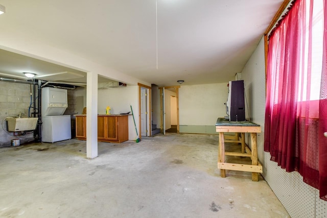 below grade area featuring a sink, stacked washer / drying machine, and concrete block wall