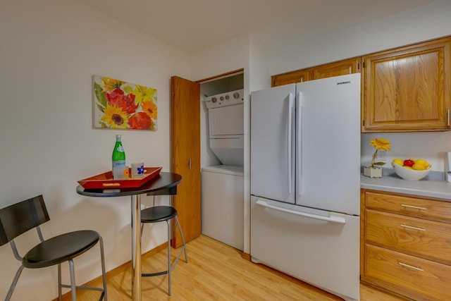 kitchen with stacked washer and dryer, freestanding refrigerator, brown cabinetry, light wood finished floors, and light countertops