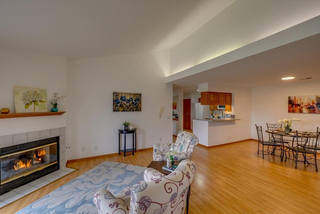 living area featuring baseboards, light wood finished floors, and a tile fireplace