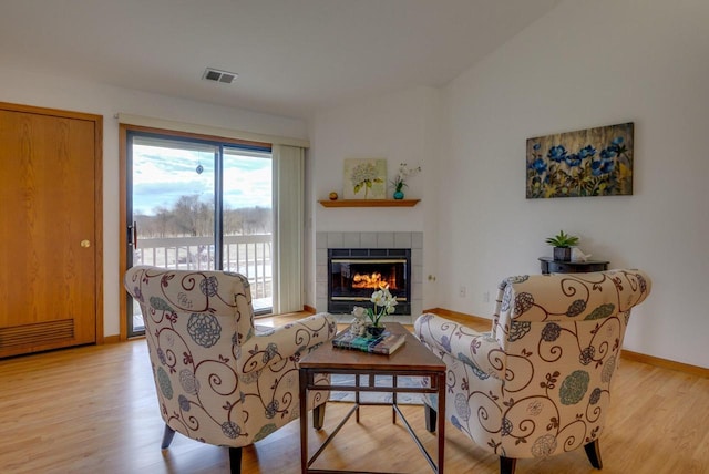 living area with light wood-style flooring, a fireplace, visible vents, and baseboards