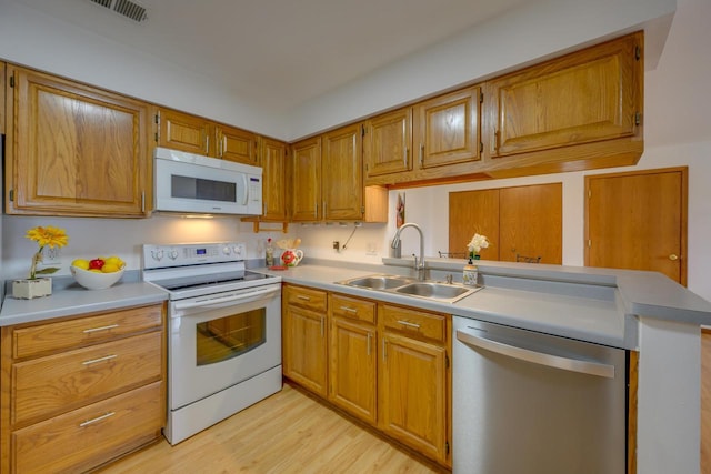 kitchen with light wood finished floors, light countertops, a peninsula, white appliances, and a sink