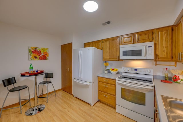 kitchen with visible vents, light wood-type flooring, a sink, white appliances, and light countertops