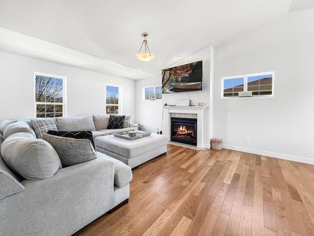 living room featuring light wood-type flooring, baseboards, a fireplace with flush hearth, and vaulted ceiling