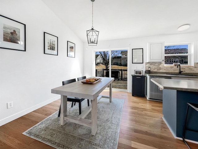 dining area featuring lofted ceiling, light wood-style floors, baseboards, and a chandelier