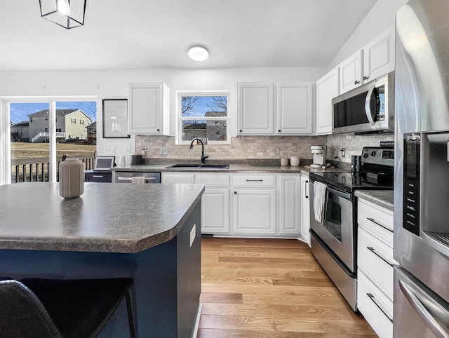 kitchen with light wood finished floors, a sink, stainless steel appliances, dark countertops, and tasteful backsplash