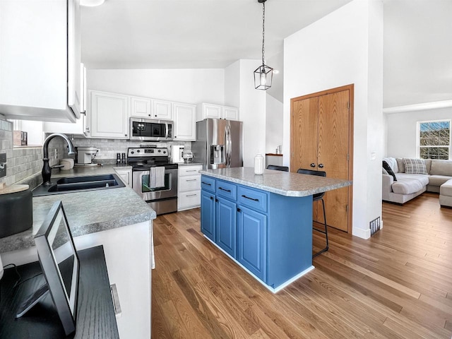 kitchen with blue cabinetry, a kitchen bar, white cabinets, stainless steel appliances, and a sink