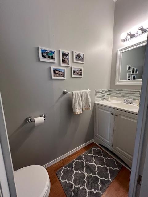 half bath with tasteful backsplash, baseboards, toilet, wood finished floors, and vanity