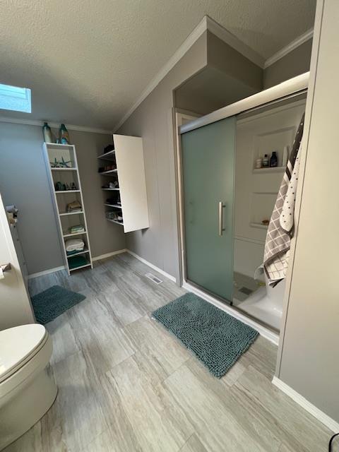 full bath with toilet, a textured ceiling, a shower stall, crown molding, and baseboards