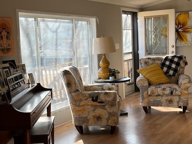 sitting room with a wealth of natural light, wood finished floors, and ornamental molding