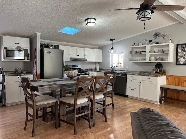 kitchen featuring light wood-type flooring, dark countertops, appliances with stainless steel finishes, white cabinets, and vaulted ceiling