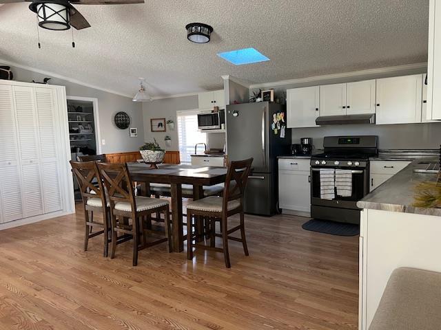 dining area featuring vaulted ceiling, light wood-style flooring, crown molding, and a textured ceiling