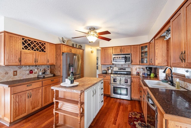 kitchen featuring a sink, glass insert cabinets, brown cabinets, appliances with stainless steel finishes, and dark wood-style flooring