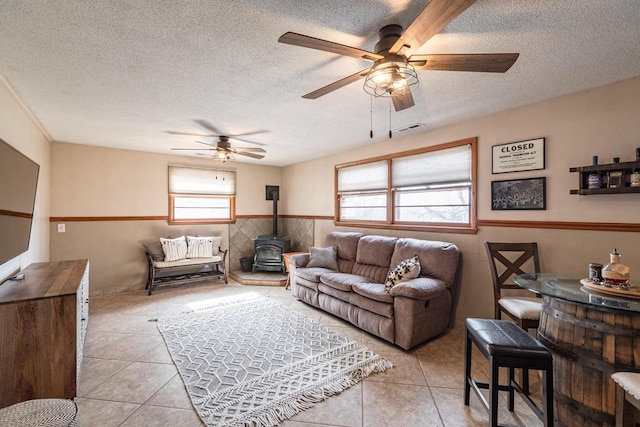 living room with visible vents, a wainscoted wall, a textured ceiling, light tile patterned floors, and a wood stove