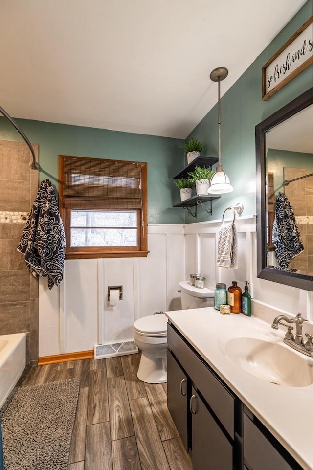 bathroom featuring toilet, shower / tub combo with curtain, wood finished floors, wainscoting, and vanity