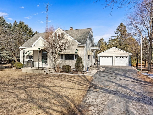 view of front of home with a shingled roof, a porch, a chimney, a garage, and an outbuilding