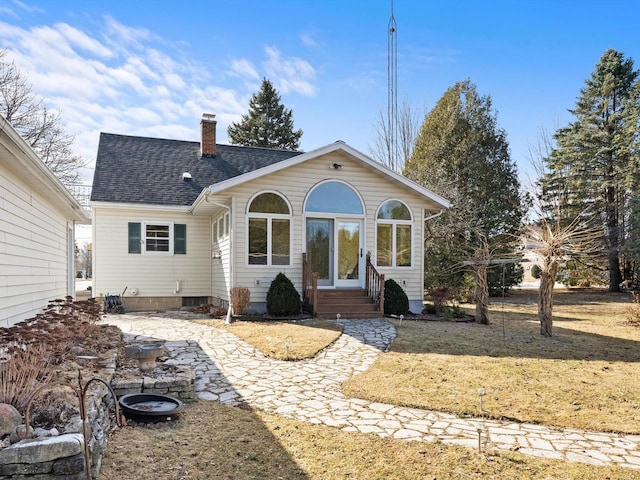 back of property with a lawn, entry steps, a chimney, and a shingled roof