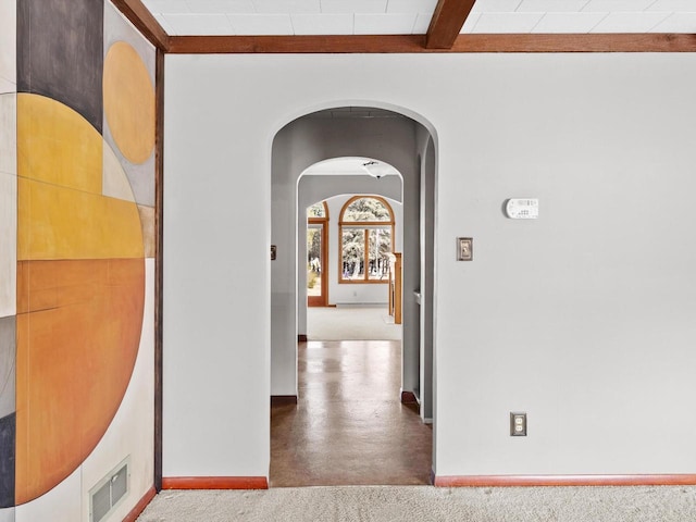 hallway with beam ceiling, visible vents, arched walkways, and baseboards