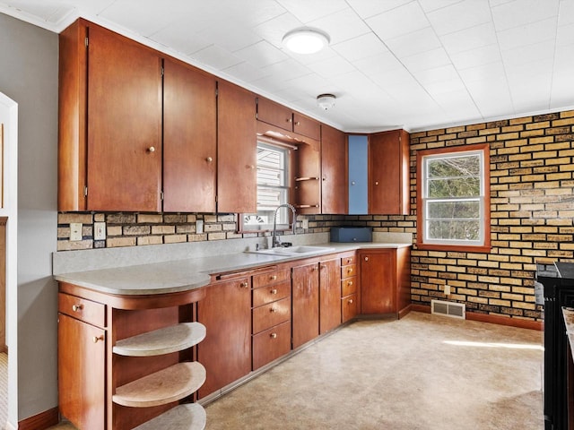 kitchen featuring a sink, visible vents, brick wall, and light countertops